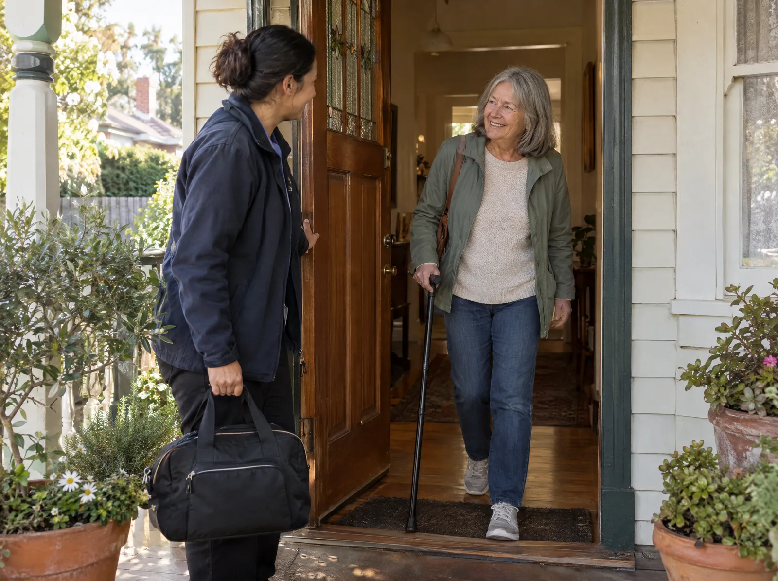 Support worker holding the front door as a woman with a cane arrives home
